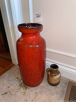 Photo showing full view of an 18-inch red pottery vase alongside a smaller 6.5-inch brown jug on a carpeted floor near a corner wall.