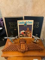 Full view of carved wooden RCAF wings badge with two metal aircraft models, magazine and atlases behind