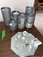 Seven grey cylindrical Swarovski collector boxes arranged in two rows on wooden surface