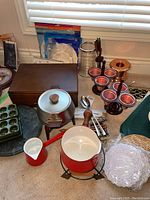 Two fondue pots (red enamel and stainless steel), fondue forks, wine chiller, copper bowl, doilies, wooden condiment stands