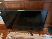 Front view of TV on stand with remote on rug