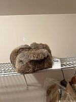 Front view of the brown and gray rabbit fur hat sitting on a white wire shelf.
