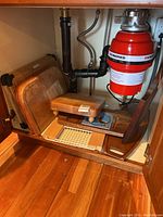 Photo inside cupboard with collection of wooden boards arranged under the sink showing cutting boards, cheese board with tile, tray, and over-the-sink board with strainer.