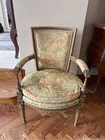 Front view showing carved wood frame, round seat cushion and floral tapestry upholstery
