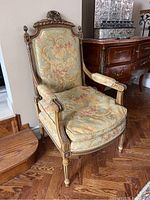 Front angled view of the vintage Louis XVI style armchair showing the floral upholstery and carved crest on the wooden frame.
