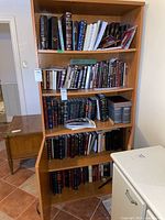 Full view of five wooden shelves filled with various Hebrew religious books and texts in hardcover and paperback formats.