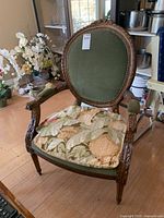 Front angle of the wood frame chair showing green fabric back, floral seat cushion, carved armrests, and wood floor.