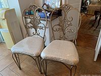 Pair of metal frame chairs with upholstered seats and decorative backs, showing overall design and height