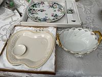 Top view of three items on table: porcelain bowl with gold handles, apple-shaped cake server in original box, and boxed cake plate with floral pattern and matching cake server.