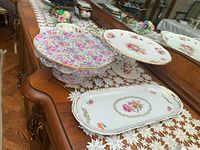 Two cake plates and a serving plate arranged on a wooden dresser with a lace cloth underneath.