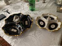 Two china serving dishes with handles on a lace tablecloth, showing the ornate gold trim, floral designs, three segmented compartments, and decorative handles.