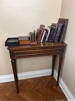 Full view of a wood console table with a drawer, showing several Hebrew books arranged on top including a leather-bound collection.