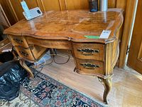Side view showing curved legs, four drawers with metal pulls, and rich wood grain with finish wear on desktop.