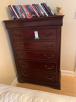 Front view of tall wooden dresser with five drawers and books on top, one drawer pull missing