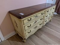 Angled side-front view showing the dresser's tapered legs, painted floral drawer details, and dark wood top.