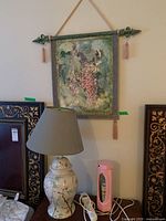 View of ceramic base table lamp with cloth shade next to hanging grapevine wall art and a pink decorative light container.