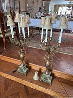 Pair of ornate Italian style gilt table lamps with fabric shades, composite and stone bases on wooden floor.