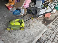Full side angle view of the Sunjoe MJ401E electric lawnmower on concrete floor with assorted garage items in background.