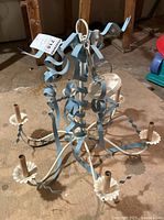 Full view of six-arm metal ceiling light fixture with curled decorative metal ribbons and candle-style sockets on a brown surface.