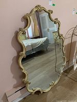 Mirror standing against a pink wall reflecting a bedroom.