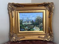 Oil painting in a highly ornate gold wood frame depicting a cottage with garden flowers and geese, wall background