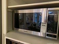Front view of Panasonic Dimension 4 The Genius microwave oven showing stainless steel body, black front window, and digital control panel with button labels visible.