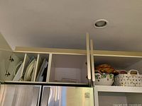 Ceramic baskets with painted fruit motif and large natural colored wicker basket on top of a cabinet shelf.