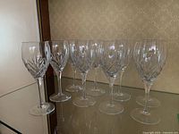 Nine Royal Doulton crystal stemware glasses arranged on a glass shelf, showing uniformity and clear crystal with distinctive cut pattern.