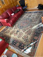 Full view of area rug under red leather sofa and office chair on hardwood floor.