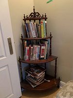 Full view of the wooden corner shelf filled with books, showing three shelves and decorative top.