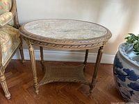 Full view of round marble top side table showing carved wood frame and wicker shelf