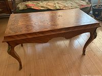 Front-side view of rectangular wood veneer table showing marquetry inlay and cabriole legs with metal mounts