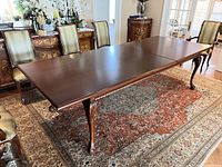 Full view of the rectangular wood dining table with polished dark brown finish and ball and claw carved legs. Shows extension leaf in place.
