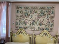 Full front view of the floral tapestry hanging above two yellow vintage-style twin bed heads in a room with peach walls and sheer pink curtains.