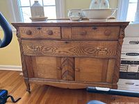 Front view of antique wooden server showing two small top drawers, one large drawer with brass handles, two cabinet doors, decorative carvings, and wood grain finish.