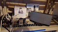 Photo of boxed Panasonic cordless phone set, Audio-Technica microphone box, Canon Powershot camera, Bose dock and cables on shelf