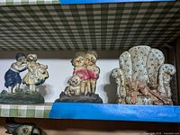 Overall view of three cast iron door stops on green checkered fabric shelf showing the group. Items visibly chipped and rusted.