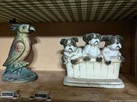 Two cast iron door stops side by side showing parrot and puppies on base shelf.