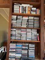 Full view of bookshelf filled with stacked music CDs and cassette tapes in various packaging states including new in package and used.