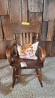 Front view of wooden child's rocking chair with angel pillow on seat against wooden background.