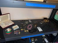 Shelf display of assorted costume jewelry including necklaces, bracelets, pins, watches, novelty dolls