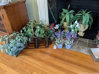 Multiple faux floral arrangements in woven baskets, urn planters, and small pots grouped on floor and hearth.