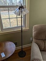 Full view of the metal floor lamp with marble base and two glass shades next to a window and a couch.