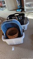 Stacked plastic laundry hampers in white and blue colors with two round rattan baskets placed inside the top hamper. Visible carpet flooring and vacuum cleaner in background.