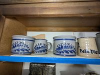 Five pieces of local stoneware including jars and a mug, showing blue floral leaf decoration and signed Bellmead and Skillman