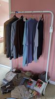 Clothing rack holding several men's jackets and pullovers mostly in neutral, brown, and blue tones. Clothing and hats placed at rack base.