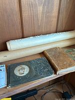 Shelf with vintage story album book featuring a young girl on the cover, two old books, and three rolled sheets of paper