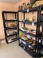 Two black plastic shelving units holding various household items like games and figurines, showing overall size and shape.