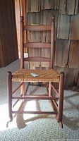 Front view of a wooden rocking chair with ladder back and woven cane seat, showing overall condition and design.
