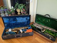 Two saxophones side by side in their cases: gold colored in blue lining and silver in green lining